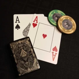 Schwarzes Feuerzeug mit Pik-Ass-Gravur, zwei Pokerkarten (Pik-Ass und Herz-Ass) sowie Pokerchips auf schwarzem Tisch