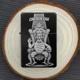 Personalisiertes Feuerzeug mit humorvollem Motiv eines gerupften Huhns als König auf einem Thron, stimmungsvoll auf einer Holzscheibe arrangiert.