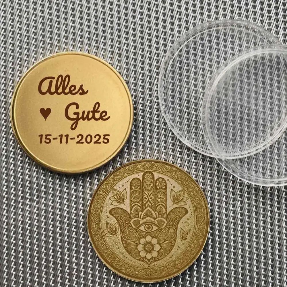 Die Hamsa-Münze liegt neben ihrer transparenten Schutzkapsel mit Beispiel Gravurtext der Rückseite.