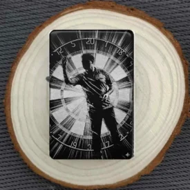 Darts Feuerzeug, Schwarz matt mit graviertem Spieler vor einer Dartscheibe, liegend auf einer Holzscheibe.