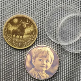 Beispiel der Münze mit optionaler Fotogravur eines Kindes auf der Rückseite statt des Text-Designs, neben der Stier-Vorderseite.